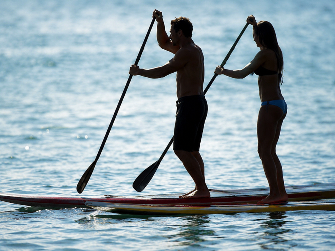 Casal praticando stand up paddle no mar ao entardecer